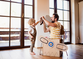 A toddler boy and father with carton plane playing indoors at home, flying concept.