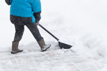 Old woman in warm blue jacket clears a snowdrifts with a snow shovel