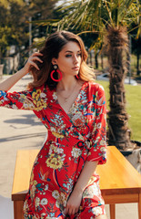 beautiful sensual woman with blond hair in elegant colorful dress relaxing in summer park