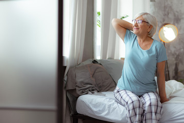 Nice-looking woman looking into the window while sitting on bed.