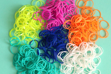 Pile of small round colorful rubber bands for making rainbow loom bracelets isolated on mint background