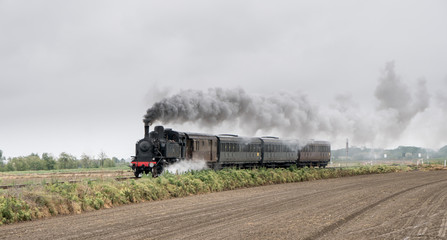 Plakat Vintage steam train with ancient locomotive and old carriages runs on the tracks in the countryside