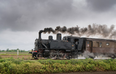 Naklejka na ściany i meble Vintage steam train with ancient locomotive and old carriages runs on the tracks in the countryside