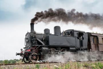 Plakat Vintage steam train with ancient locomotive and old carriages runs on the tracks in the countryside