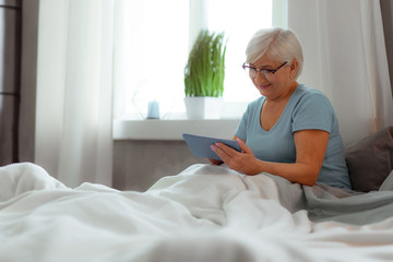 Smiling female clicking on the tablet while lying in bed