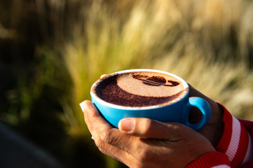 Woman hands holding blue cup of hot chocolate with cocoa powder Saturn shape decoration in blur...