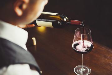 Close up shot of sommelier pouring red wine from bottle in glass