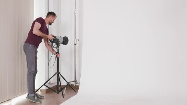 Fashion photographer setting up flash lights in the studio next to a big white background