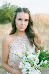 Fototapeta na wymiar Beautiful young bride with long hair in a wedding dress with a bouquet in the summer in the field