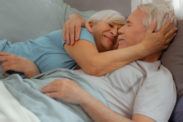 Loving wife tenderly hugging her spouse while lying with him
