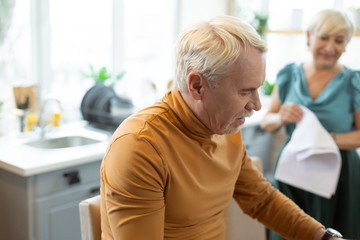 Fototapeta premium Stylish handsome attractive grey-haired bearded man sitting at the kitchen.