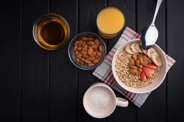Oatmeal cereal. Natural healthy food. Morning meal. Juice, honey, nut, strawberry, banana, coffee on black background