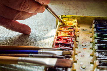 artist's tools, professional watercolor paints in a box, artist's brushes and brushes on a bright old table, soft focus