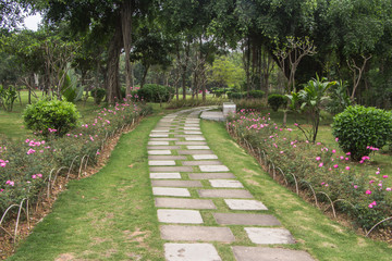 In the summer park, there is a stone paved stone road under the wood that bends out into the distance.