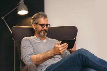 middle aged man using tablet sitting in sofa at his home