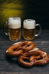 tasty pretzels on dark wooden background with draft beer in the mug in blurred background