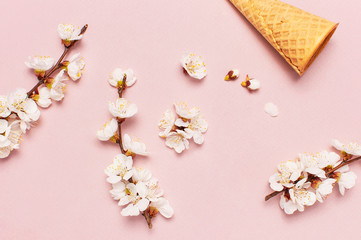 Obraz na płótnie Canvas Waffle cone with bouquet of spring blooming branches of white flowers on pastel pink background. Creative spring minimal concept. Flat lay top view copy space.