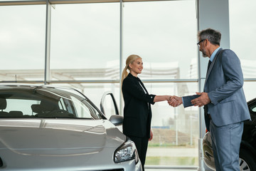 sales agent shaking hand with customer in car dealership showroom