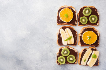 Sandwiches with chocolate paste and various fruits on a gray table. Top view. Concept delicious Breakfast. Copy space