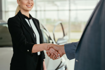 closeup of sales agent shaking hand with customer in car dealership showroom