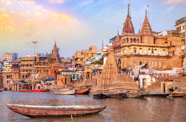 Ancient Varanasi city architecture with view of wooden boat on river Ganges at sunset