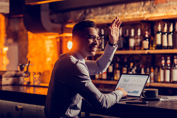 Freelancer sitting at the bar stand with laptop waving his friend