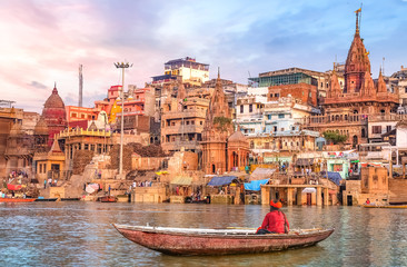 Ancient Varanasi city architecture at sunset with view of sadhu baba enjoying a boat ride on river Ganges.