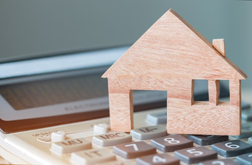 Wooden house model on calculator for budget payment or buying home. Ideas for property real estate...