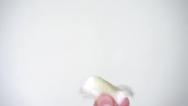female hands on a white background are holding a cotton pad and drench it with green nail polish remover without acetone