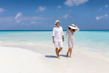 Happy couple walks down a tropical beach with turquoise sea and sunshine