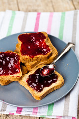 Fresh toasted cereal bread slices with homemade cherry jam and spoon on ceramic plate closeup on linen napkin on rustic wooden table background.