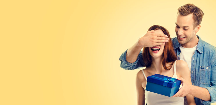 Photo of happy couple with gift box, closed eyes, over yellow color background