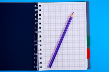 Top view of open spiral blank notebook with pencil on blue desk background