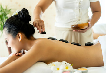 Obraz na płótnie Canvas Beautiful Young Asian woman enjoying a hot stone treatment in spa salon. relaxing and rejuvenating procedures or Leisure. lifestyle beauty woman concept. side view