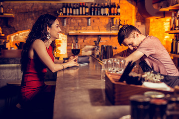 Curly woman in red dress laughing while speaking with barman