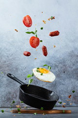 Fried egg flying in motion. Fried egg and smoked sausages on a cast iron pan with salt and spice,...