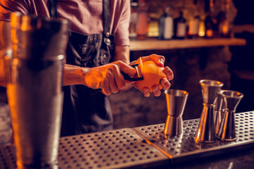 Bartender in black apron taking orange peel for cocktail