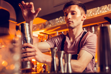 Handsome barman feeling involved while making cocktail for client