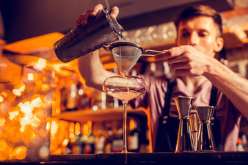 Dark-haired bartender using sieve while making cocktail