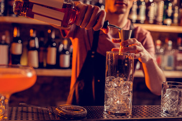 Barman wearing uniform pouring alcohol into glass with ice