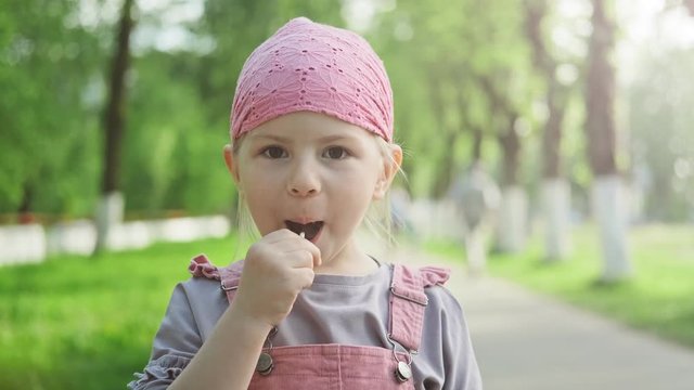 Little girl enjoying lollipop and looking at camera. Child in pink sundress eating candy