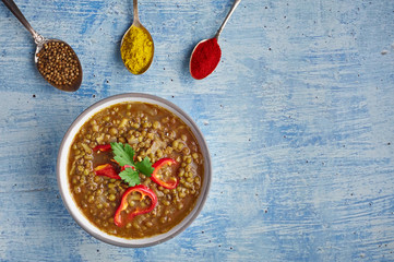 Mung Dhal decorated with red pepper slices at blue tabletop. Moong Dal - Indian Cuisine curry. Vegetarian dish with mung beans, zira cumin, coriander, curcuma and chili. Top view with copy space
