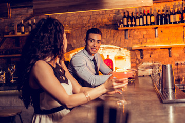 Curly woman drinking cocktail in bar talking to man
