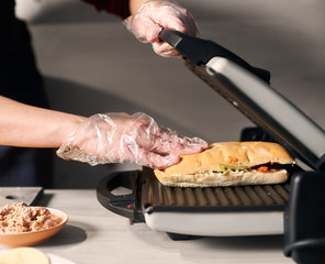 Using special grill equipment in cooking original american street popular food. Detailed of chef baking gourmet sandwich. Process of cooking typical italian refreshments. Gray background. Side view.