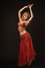 Young beautiful exotic eastern women performs belly dance in ethnic red dress on gray background. Studio shot