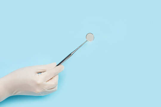Mano con guante de l&aacute;tex sosteniendo un espejo dental sobre fondo celeste liso y aislado. Vista de frente. Copy space. Concepto: Salud