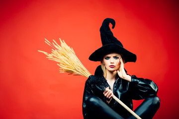 Emotional young women in halloween costumes on party over red background with pumpkin. Witch broom...