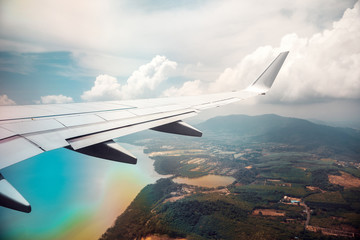 Wing of airplane in cloudy sky with rainbow effect