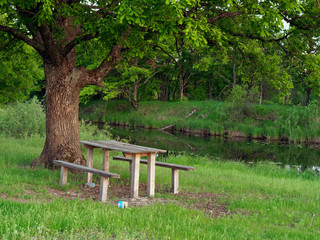 sitting area with a table and a bench by the river in the evening on a green background