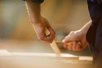 Close up of unrecognizable carpenter carving wood while working in joinery lit by sunlight, copy...